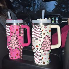 two mugs sitting in the back seat of a car with pink and white designs on them