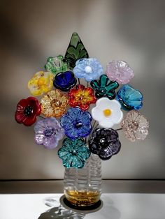 a vase filled with lots of different colored glass flowers on top of a white table