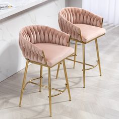 two pink velvet bar stools with gold legs in front of a marble countertop