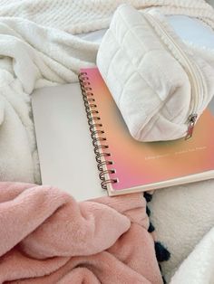 an open notebook sitting on top of a bed next to a pile of white blankets