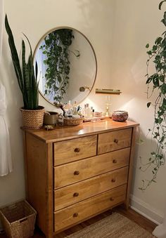 a wooden dresser topped with a mirror next to a potted plant and wicker basket