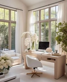 a home office with white furniture and flowers in vases on the desk, along with large windows