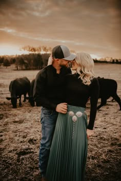 a man and woman standing next to each other in front of cows on a field