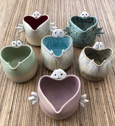 six ceramic bowls with faces and eyes on them sitting on a table together in the shape of hearts