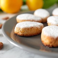 several powdered sugar cookies on a plate with almonds and lemons in the background