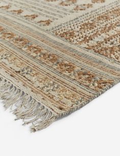 a beige and brown rug with fringes on the bottom, in front of a white background