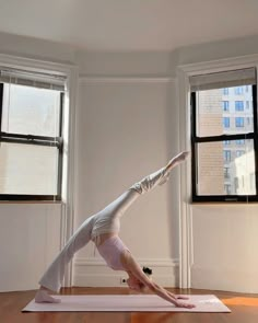 a woman is doing yoga on a mat in front of two windows with no curtains