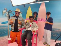 three men are sitting in chairs with surfboards behind them and one man is giving the thumbs up