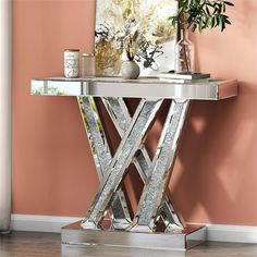 a mirrored table with silver metal legs in front of a pink wall and potted plant