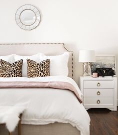 a bedroom with white bedding and leopard print pillows on the headboard, along with two nightstands