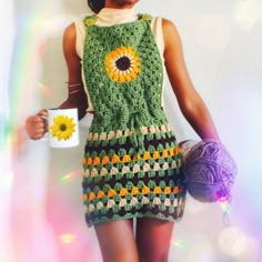 a woman is holding a mug and wearing a crocheted dress with sunflowers on it