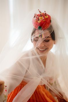 a woman wearing a veil with a red hat on top of her head and an orange dress underneath