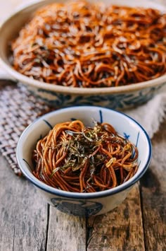 two bowls filled with noodles on top of a wooden table next to another bowl full of noodles