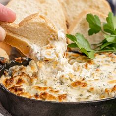 a hand dipping some bread into a skillet filled with melted cheese and parsley