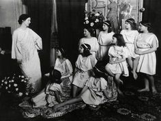 an old black and white photo of women dressed in roman garb with flowers on the floor