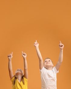 two young children standing in front of an orange background with their arms up and hands raised