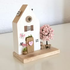 a small white house with pink flowers in the front and behind it on a wooden stand