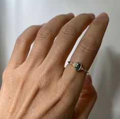 a woman's hand wearing a ring with a green stone on the middle of it