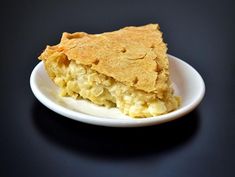 a piece of pie on a white plate sitting on a black table top next to a fork