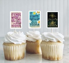 three cupcakes with white frosting on top of each one and some books in the background