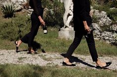 two women walking in front of a statue and grass area with rocks on the ground