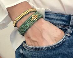 a man wearing a green bracelet with gold beads on his left wrist and jeans in the back pocket