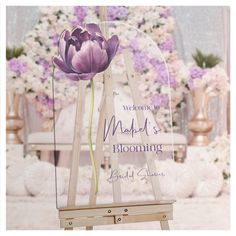 a purple flower sitting on top of a wooden easel next to a floral display