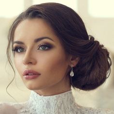 a close up of a woman wearing a white dress and earrings with her hair in a bun