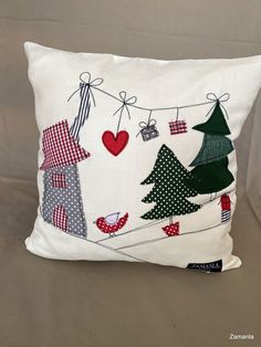 a white pillow with christmas trees on the front and red heart hanging from it's back