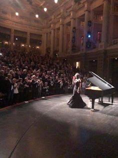 a woman standing on top of a stage next to a piano in front of an audience