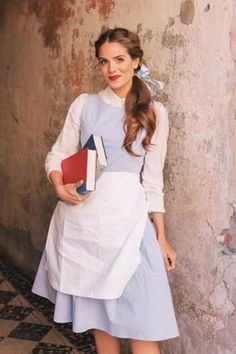 a woman standing next to a wall wearing a dress and holding books in her hands