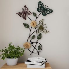 a metal wall sculpture with flowers and butterflies on it next to a potted plant