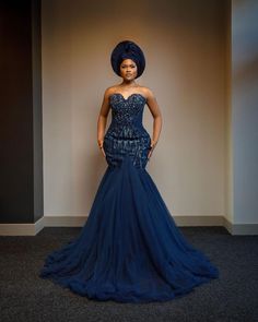 a woman in a blue dress and turban standing next to a white wall