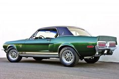 a green mustang muscle car parked in front of a white wall