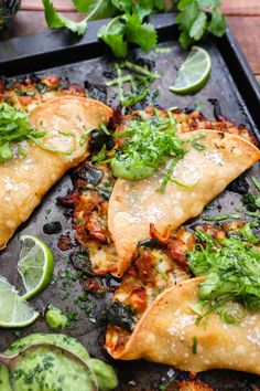 some tacos are on a tray with cilantro, limes and sour cream