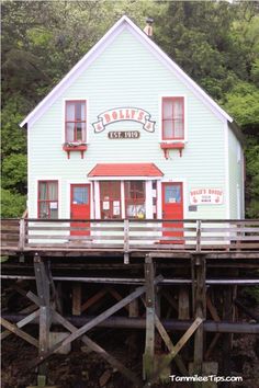 a white building with red doors and windows on the side of a dock in front of some trees