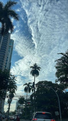 a car is driving down the street in front of tall buildings with palm trees on both sides