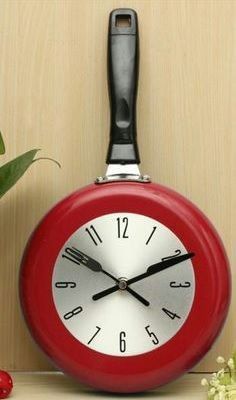 a red clock sitting on top of a table next to a pot with flowers in it