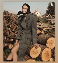 a woman sitting on top of a pile of logs wearing a gray coat and black boots