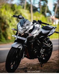 the motorcycle is parked on the side of the road in front of some trees and bushes