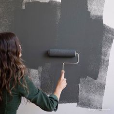 a woman is painting the wall with gray paint