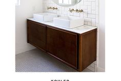 a bathroom with two sinks and a round mirror above it's countertop, in front of a white tiled wall