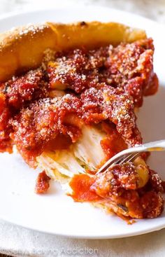 a piece of deep dish pizza on a white plate with a fork in the foreground