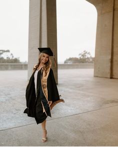 a woman in a graduation gown and cap is posing for a photo under the bridge