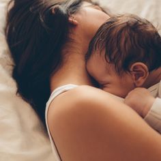 a woman laying on top of a bed holding a small child in her arms,