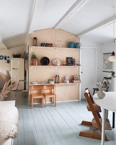 an open kitchen and dining room area with white walls, wood flooring and shelving