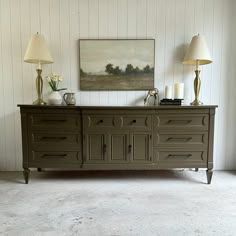 a dresser with two lamps on top of it and a painting hanging above the drawers