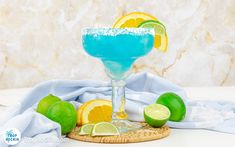 a blue margarita cocktail with limes and lemon wedges on a white tablecloth