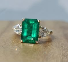 an emerald and diamond ring sitting on top of a wooden table