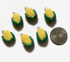 six small corn on the cob charms next to a penny